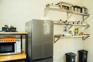 A kitchen with a stainless steel refrigerator, a microwave, and shelves above holding various kitchen items.