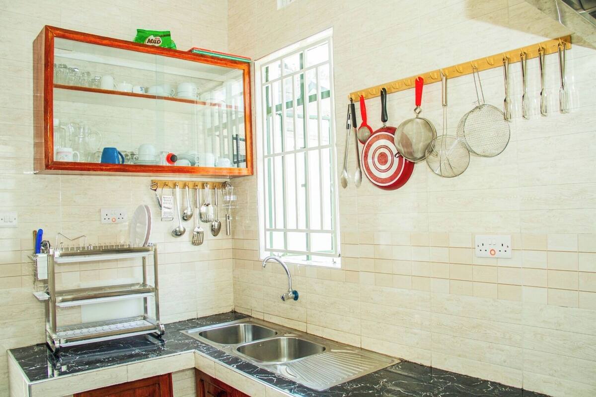 A kitchen with a sink, a mirror, and utensils hanging on the wall.