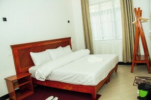 Una cama bien hecha con cabecera y mesita de noche de madera, y un par de zapatillas en el suelo.