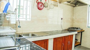 Cozinha com bancada de mármore, armários de madeira e pia de aço inoxidável, com panelas penduradas.