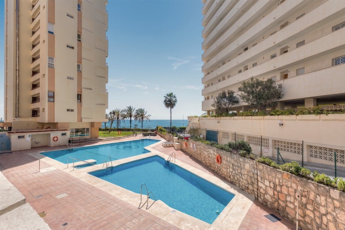 A rooftop swimming pool with a clear view of the sea, surrounded by high-rise buildings.