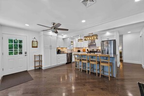 Une cuisine moderne avec des meubles blancs, un îlot central doté de tabourets, un ventilateur de plafond et un éclairage encastré.