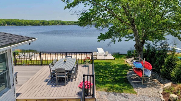 A deck with a table and chairs, a dock, and a boat. - Heron's Rest – Lakefront Home w/ Hot Tub, Kayaks & Game Room (Pocono Lake)