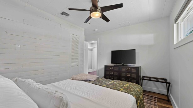 Un dormitorio con cama, cómoda, televisor y ventilador de techo.