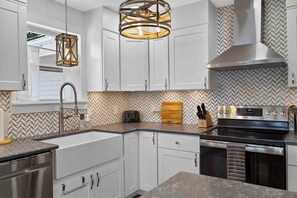 Uma cozinha moderna com armários brancos, um backsplash em padrão herringbone e um exaustor de aço inoxidável, além de um forno embutido.