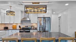 Una cocina moderna con una isla grande, electrodomésticos de acero inoxidable y una lámpara colgante original.