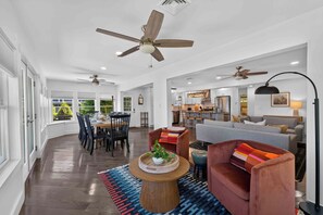 Ein großzügiger Wohnbereich mit Esstisch, Sofas, Deckenventilatoren und einer Küche im Hintergrund.