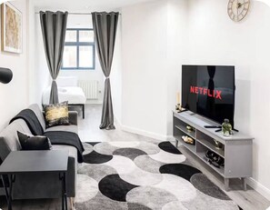 Een moderne woonkamer met een bank, een televisie, een salontafel, een vloerkleed met dessin en een minimalistische inrichting.