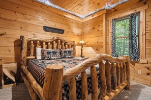 Ein Schlafzimmer einer Holzhütte mit einem Bett, einem Nachttisch, einer Lampe und einem Fenster mit Vorhängen.