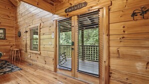 Interior d'una cabana de fusta amb terra de fusta, una porta de fusta amb reixatge metàl·lic, una banca de fusta i una paret de fusta amb un rellotge.
