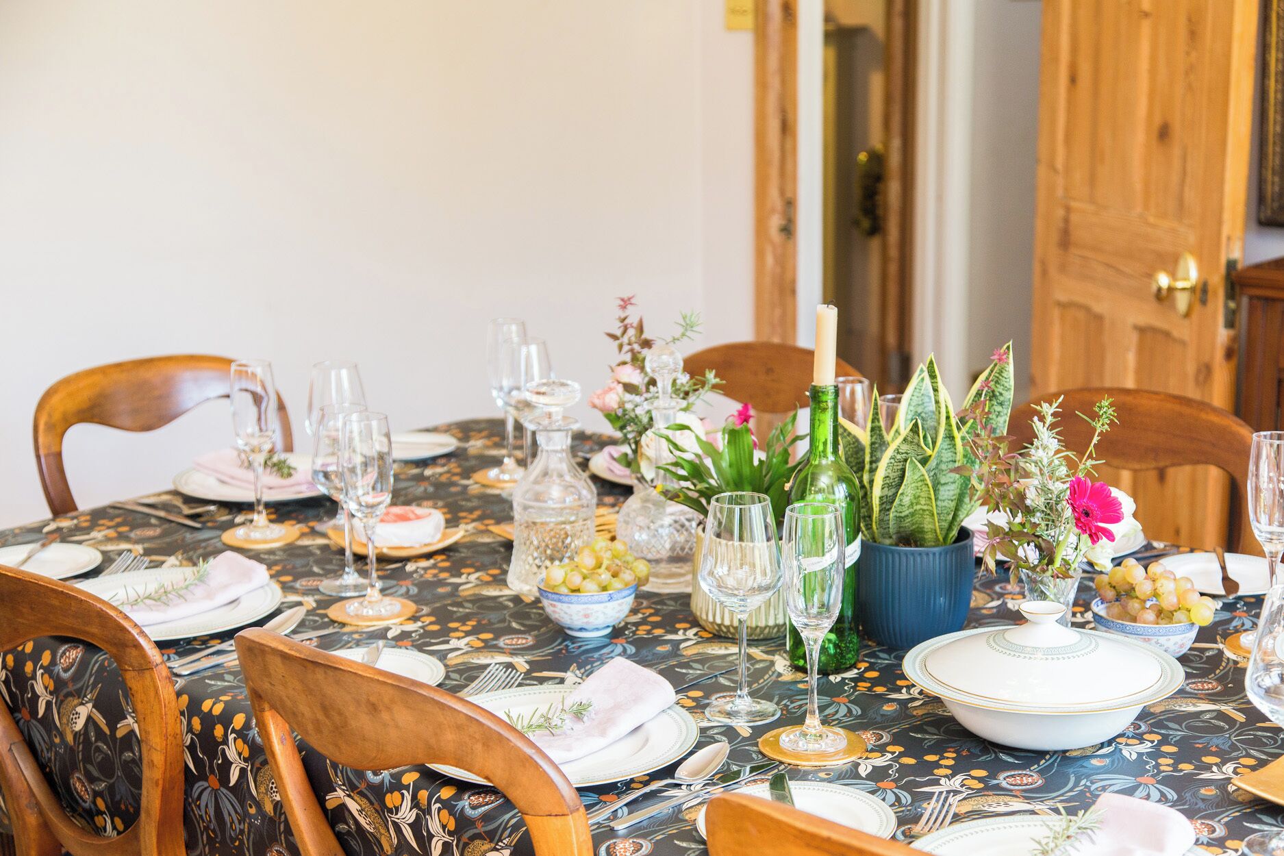 Ett matbord dukat med tallrikar, glas och en mittdekoration bestående av blommor och ett ljus.
