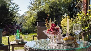 A round glass table with wicker chairs, a bowl of strawberries, a candle, and a bottle of wine.