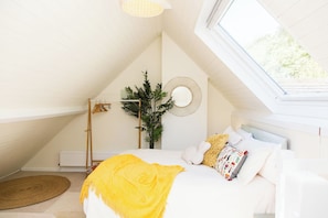 A bedroom with a sloped ceiling, a bed with white bedding, a yellow throw blanket, a window, and a wall-mounted mirror. - Whitebeams (Canterbury)