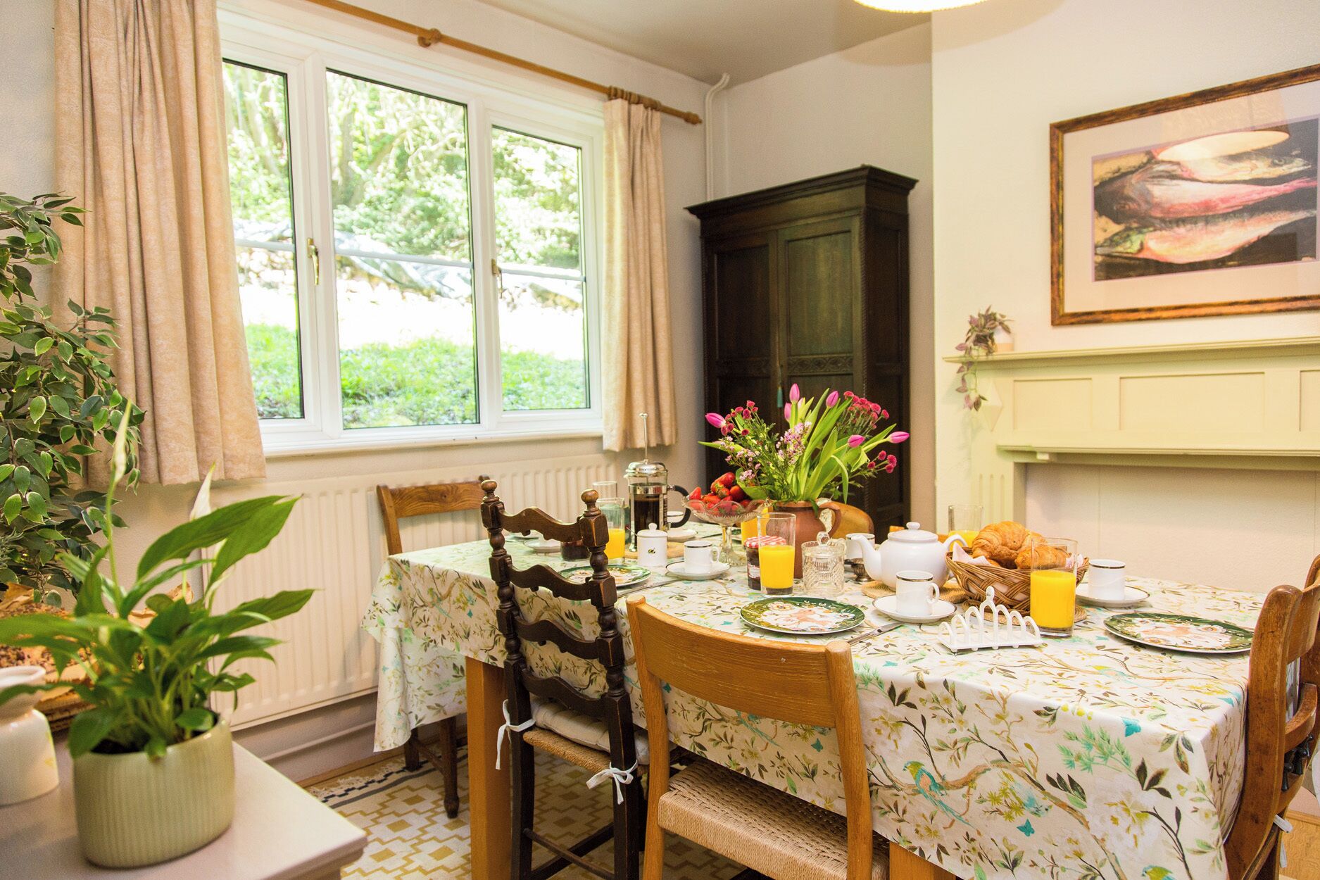 A dining area with a table set for breakfast, including a croissant, orange juice, and a vase of flowers.