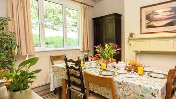 A dining area with a table set for breakfast, including a croissant, orange juice, and a vase of flowers.