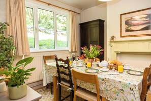 Un comedor con una mesa dispuesta para el desayuno, que incluye un croissant, jugo de naranja y un florero con flores.