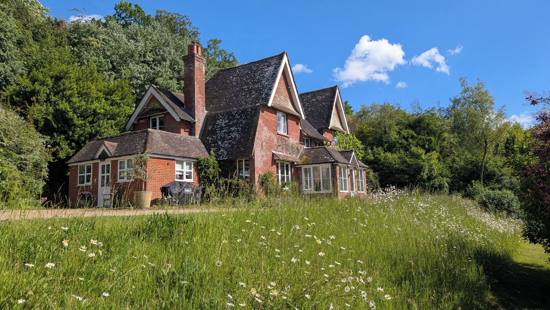 A large house with multiple rooms, surrounded by a lush garden and trees.