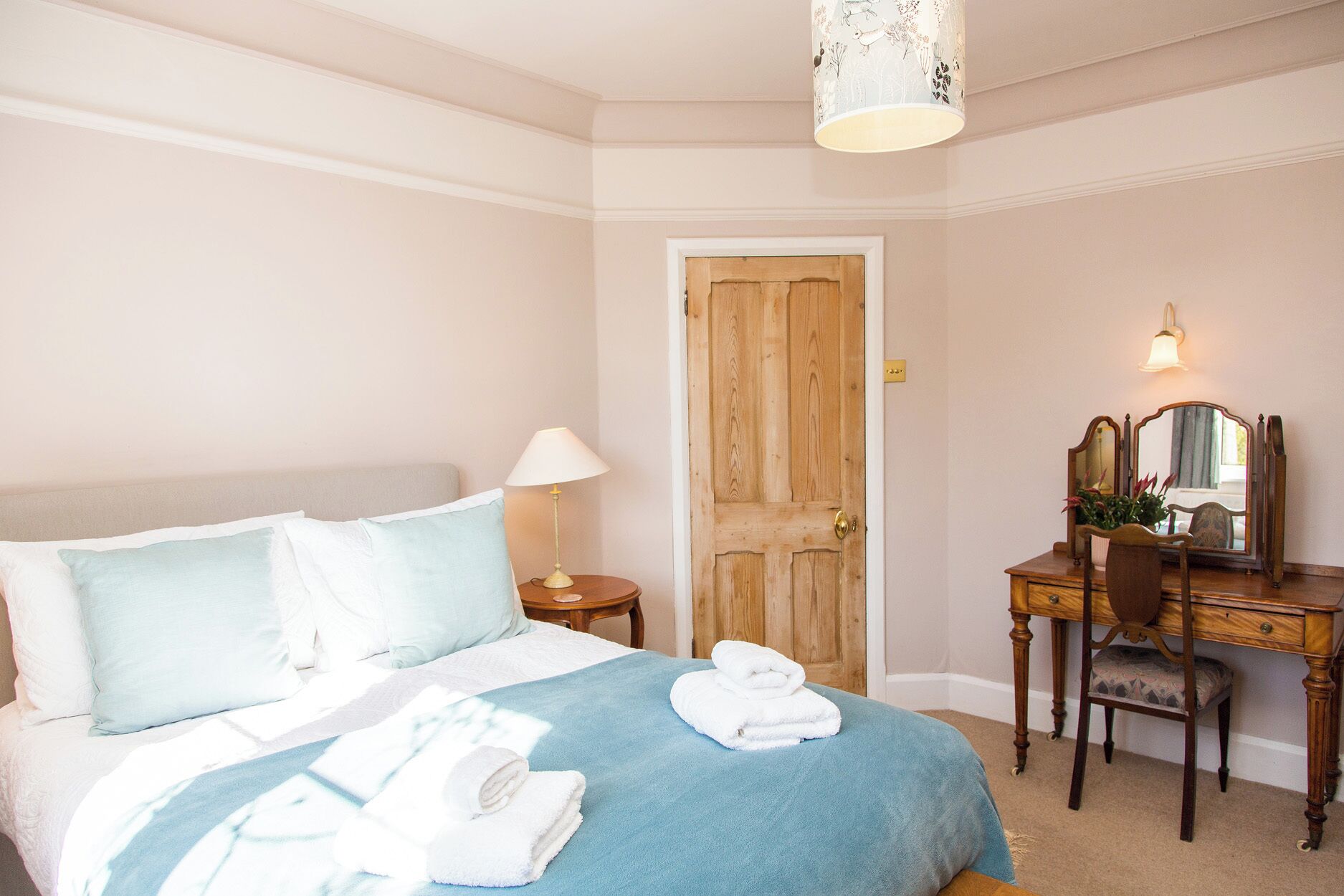 A bedroom with a bed, a desk with a mirror, and a door.