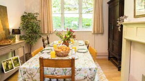 Ein Esszimmer mit gedecktem Tisch für das Frühstück, einem Fenster mit Vorhängen, einer Pflanze und einem Kamin.