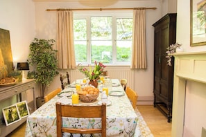 Ein Esszimmer mit gedecktem Tisch für das Frühstück, einem Fenster mit Vorhängen, einer Pflanze und einem Kamin.