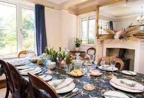 Ein Esszimmer mit einem großen Esstisch, gedeckt für eine Mahlzeit, Stühlen, einem Spiegel und einem Kamin.