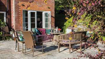 A patio with wicker furniture, a table with drinks, and a brick building with a window.