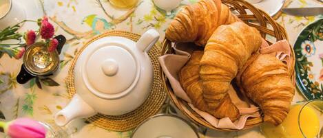 A breakfast setting with croissants, a teapot, cups, and a glass of orange juice.