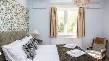 A bedroom with a bed, a chair, a window with curtains, a radiator, and a chandelier.