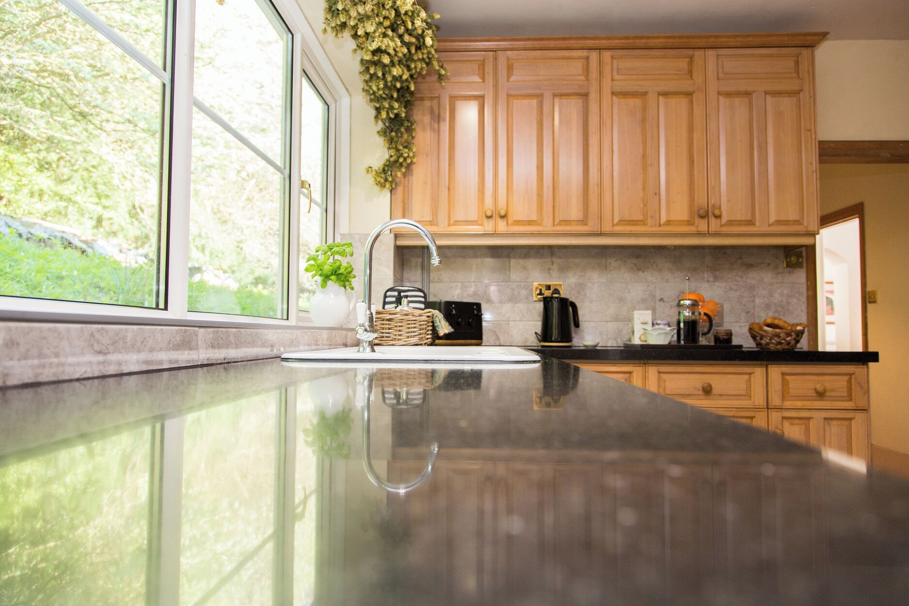 A kitchen with wooden cabinets, a stainless steel sink, and a window with a view of greenery.
