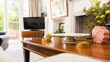 A living room with a wooden table, a television, and a pink vase with flowers.