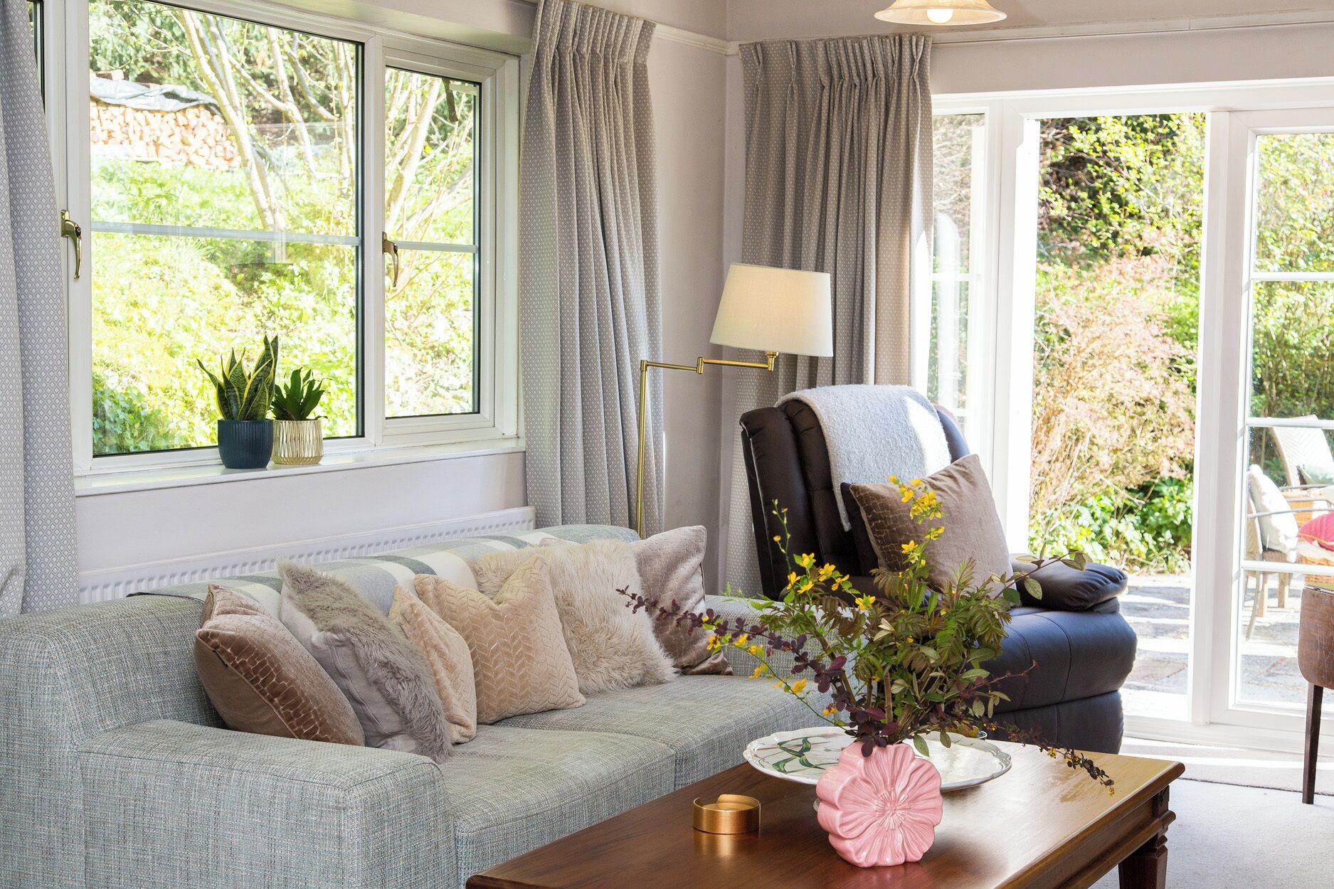 A cozy living room with a sofa, a chair, a table with a vase, and a lamp.