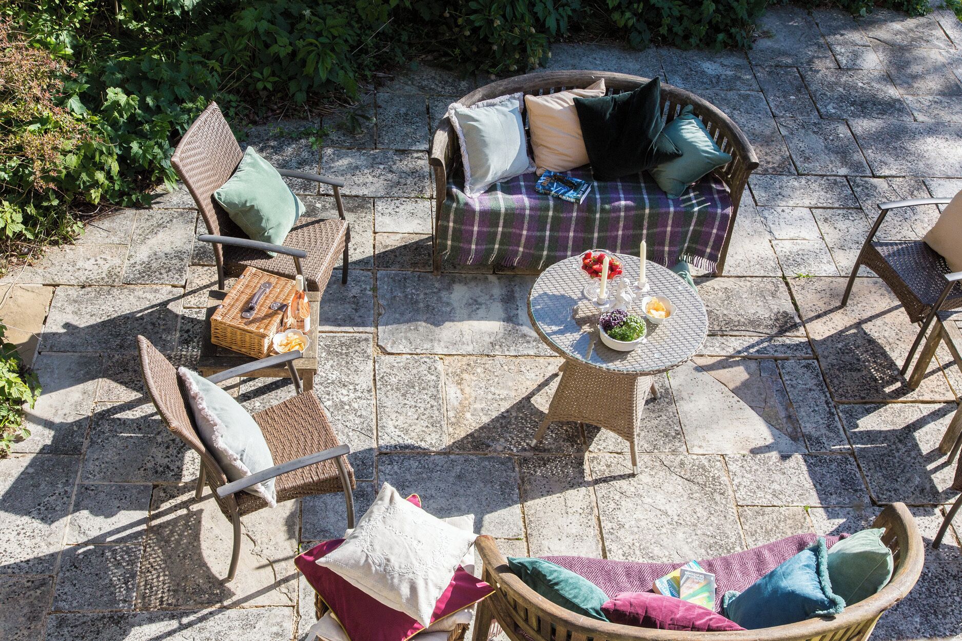 A patio with wicker furniture, a round table with a bowl and candles, and a stone floor.