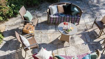 A patio with wicker furniture, a round table with a bowl and candles, and a stone floor.