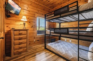 Ein Schlafraum mit Etagenbetten, einem Fernseher an der Wand, einem Tisch mit Lampe und Holzwänden.