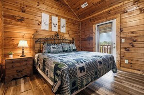 Ein Schlafzimmer einer Holzhütte mit einem Bett, einem Nachttisch, einer Lampe und einem Fenster mit Jalousien.
