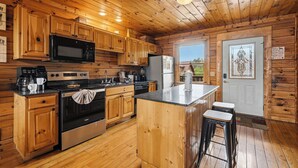 Una cocina de estilo cabaña de madera con una isla central, electrodomésticos de acero inoxidable y armarios de madera.
