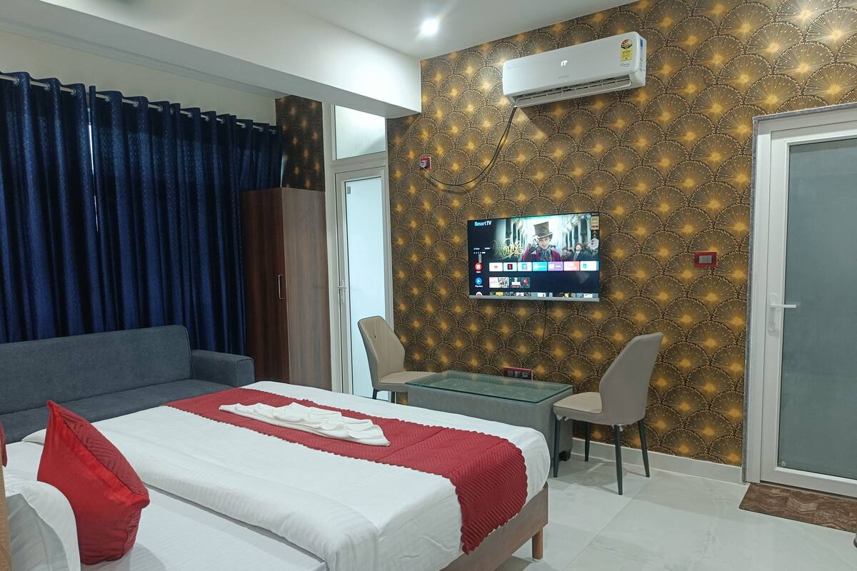 A hotel room with a bed, a TV, a sofa, a table, and a door.