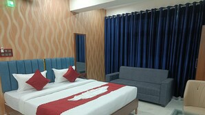 Una habitación de hotel con una cama, un sofá gris, una mesa de centro de cristal y una cortina azul.