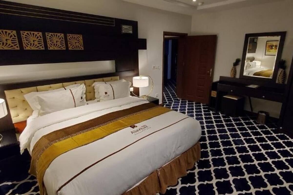 A hotel room with a bed, bedside tables, a dresser, a mirror, and a patterned floor.