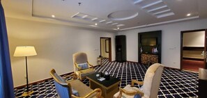 A hotel room with a check-in desk, two armchairs, a sofa, a lamp, a television, and a patterned floor. - ALAZHAR PALACE HOTEL (Qunfudhah)