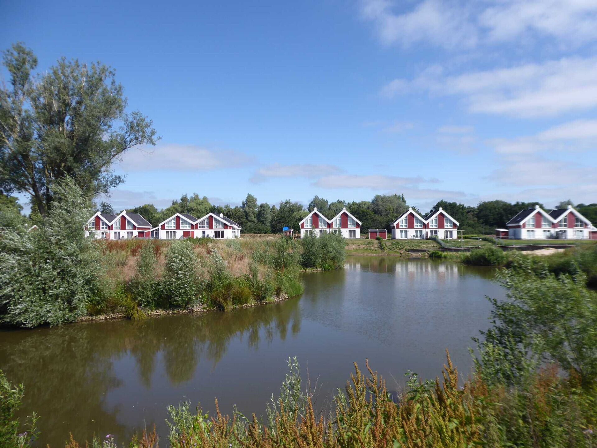 Een rij rode en witte huizen aan een rustig meer, omringd door groen.