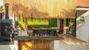 Ein Essbereich im Freien mit einem Reetdach, einer Grillstation und Blick auf den Garten.