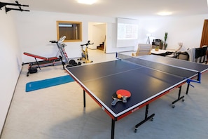 A ping pong table with a net, exercise equipment, and a projector screen in a room with a white wall and a door. - Luxury Vacation Seaside Villa With Privacy (Çeşme)