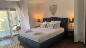 Ein modernes Schlafzimmer mit einem großen Bett, zwei Nachttischlampen, einem Wandbehang aus Makramee und Blick durch eine Glastür.