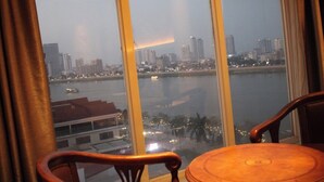 A room with a large window overlooking a cityscape and a body of water. - Gold Indigo Hotel (Phnom Penh)