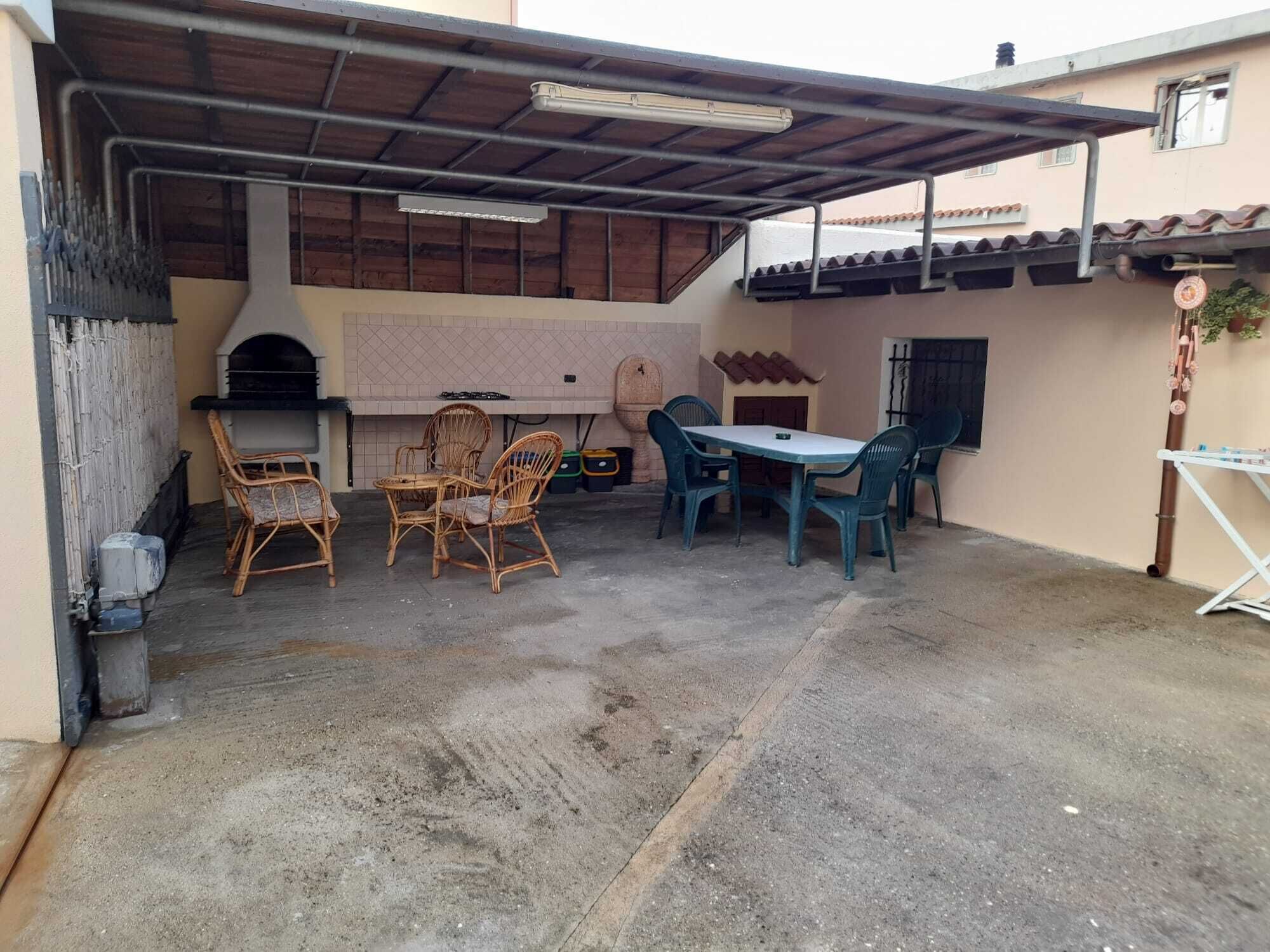 An outdoor patio with a grill, wicker chairs, a table, and a covered area.