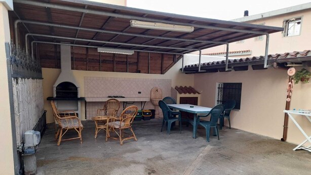 Eine Terrass mit Grill, Korbmöbeln, einem Tisch und einem überdachten Bereich.