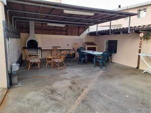 An outdoor patio with a grill, wicker chairs, a table, and a covered area. - Martineriu House (Orosei)