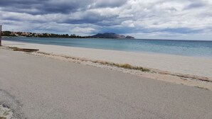Ein Strand mit gepflastertem Weg, ruhiger See und fernen Bergen unter bewölktem Himmel.