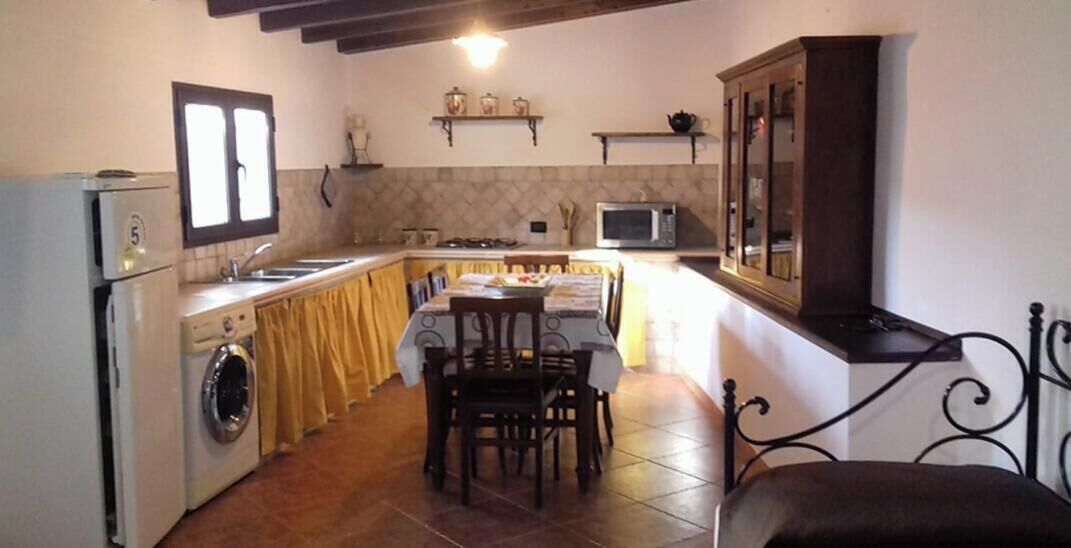 A compact kitchen with a dining table, chairs, a washing machine, a microwave, and a cabinet.